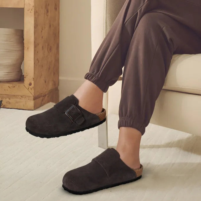 Woman wearing Aerothotic Atlas suede clogs, seated indoors in a fall outfit