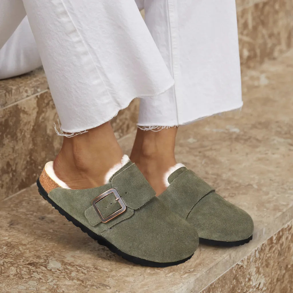 Green suede slippers with a buckle worn indoors on a stone floor.
womens comfort clogs