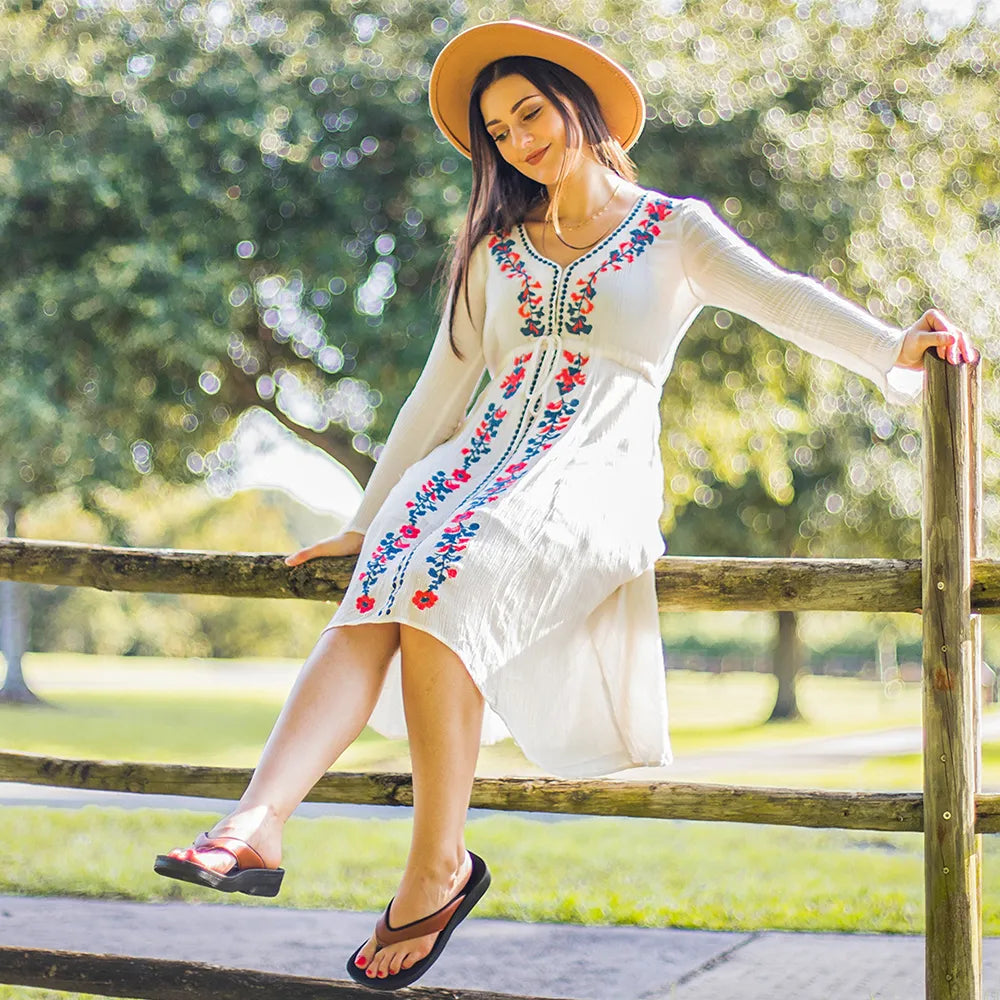 Woman in a white dress with floral embroidery sitting on a wooden fence in a park.
arch support thongs