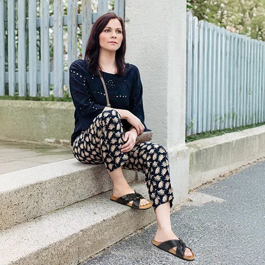 Woman sitting on steps wearing a navy top and patterned pants with a light blue fence in the background
cork sandals
cork sandals womens
cork bed sandals women
